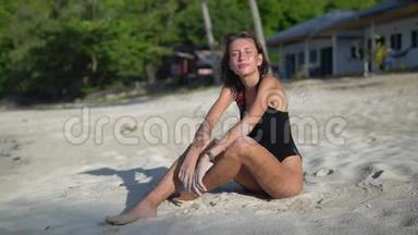 <strong>照片</strong>中，一个皮肤黝黑的皮肤苗条的女人穿着一件被隔离在沙滩上的黑色<strong>泳装</strong>，正对着镜头摆姿势